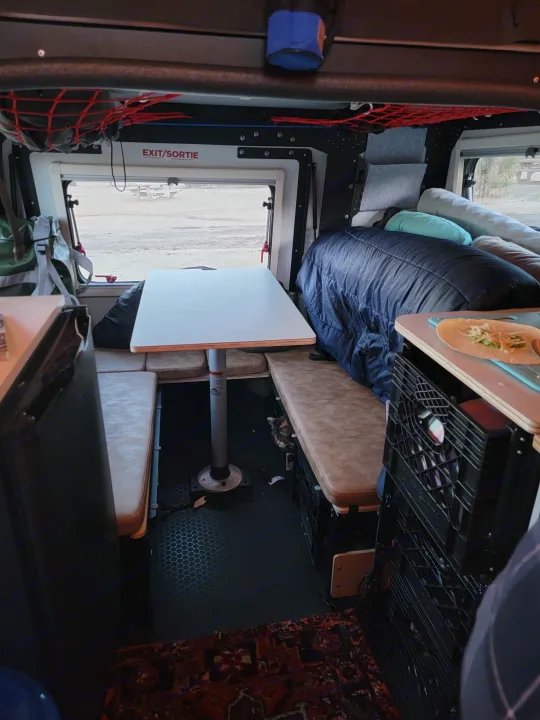 Spacious RV rental interior with a cozy dinette, sleeping area, window view, and a cat under the table.. TAXA Habitat Mantis 2021