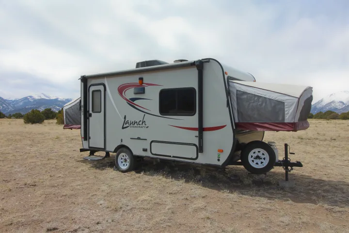 Compact pop-out RV rental travel trailer set up for camping in a dry, mountainous landscape.. Starcraft Launch 2016