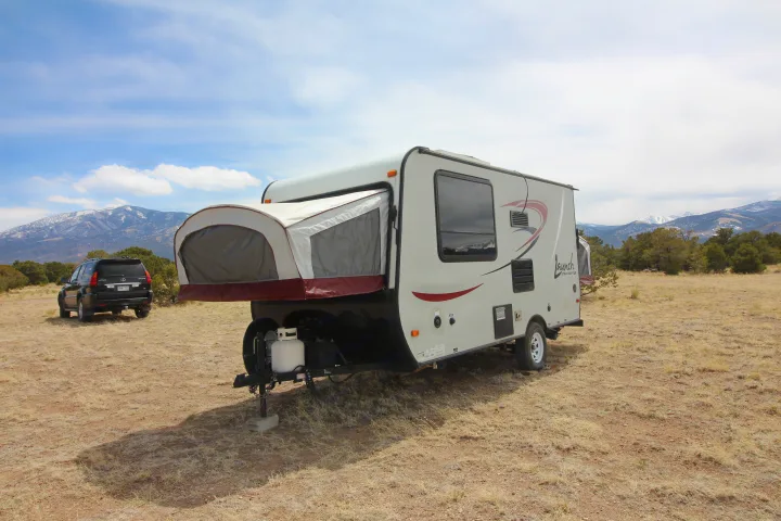 An RV rental, a Starcraft Launch travel trailer with an expanded bed, sits in a dry field, with a black SUV and mountains beyond.. Starcraft Launch 2016