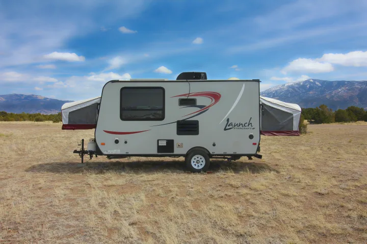 RV rental: A grey hybrid travel trailer with expanded bed ends in a dry field, mountains behind. Great for camping!. Starcraft Launch 2016