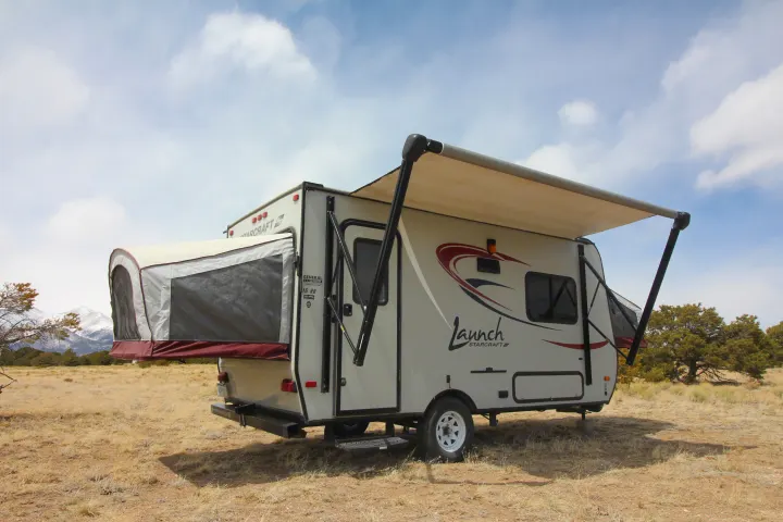 A Starcraft Launch hybrid rv rental, set up with awning in a dry field. Snowy mountains and trees define the scenic camping backdrop.. Starcraft Launch 2016