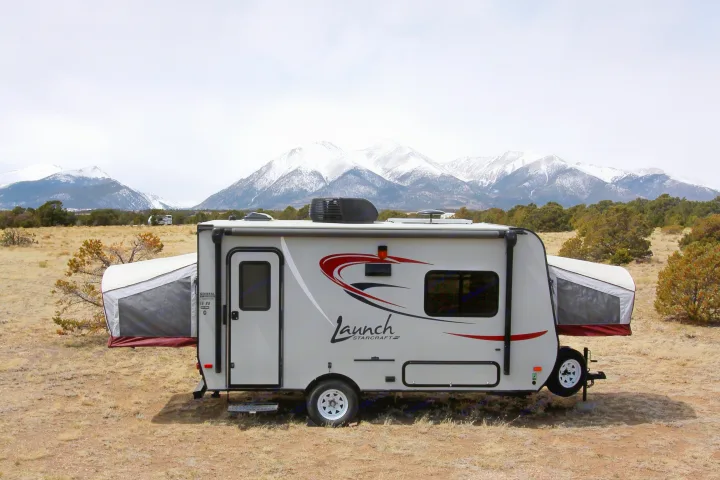 Experience nature with an RV rental: A pop-up travel trailer in a vast, dry landscape under snowy mountains.. Starcraft Launch 2016