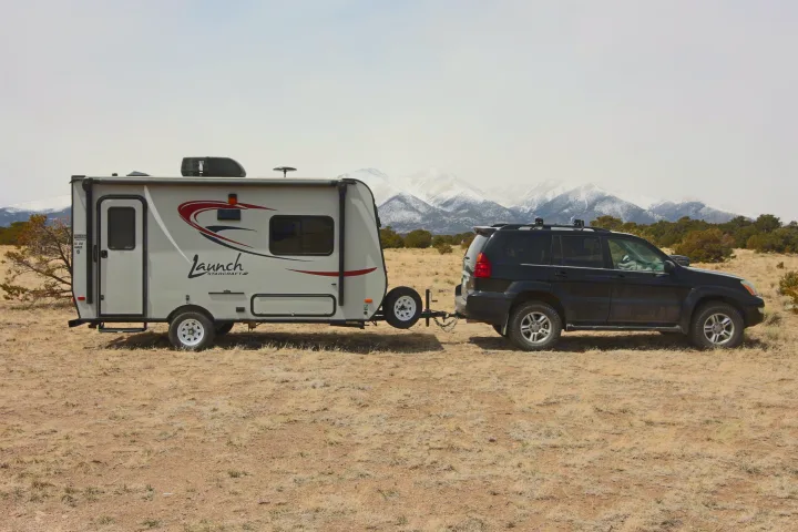 Black SUV towing an RV rental travel trailer through a dry landscape, with snow-capped mountains in the background. Ready for adventure.. Starcraft Launch 2016