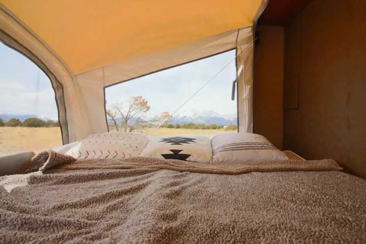 View from inside an RV rental bed, cozy with a fluffy blanket & pillows, overlooking a field and snowy mountains.. Starcraft Launch 2016