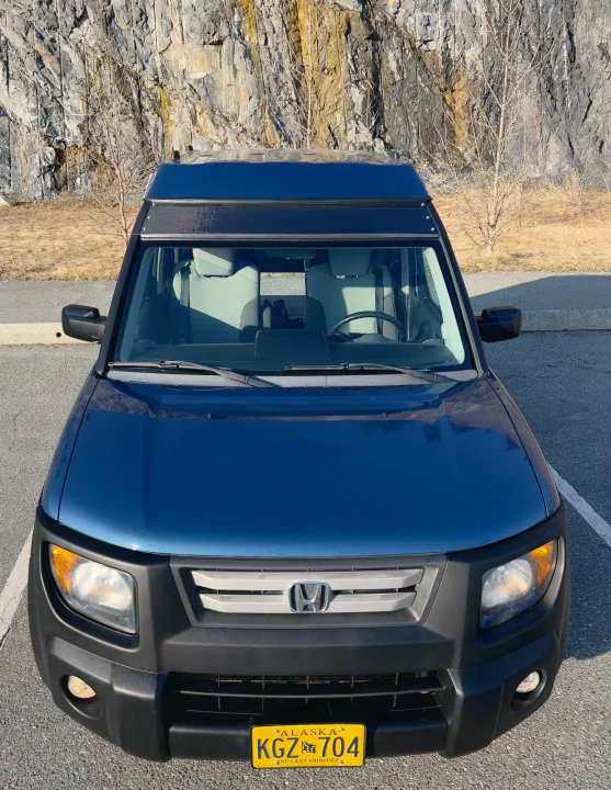 Elevated view of a blue Honda Element RV rental featuring a pop-top roof. Parked by a rocky cliff in Alaska.. Honda Element Ecamper 2008