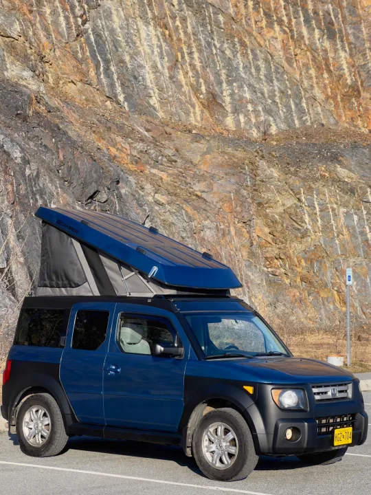 A blue Honda Element with an ECamper pop-top, a compact RV-style camper, parked by a rocky cliff. Perfect for unique rv rental trips.. Honda Element Ecamper 2008