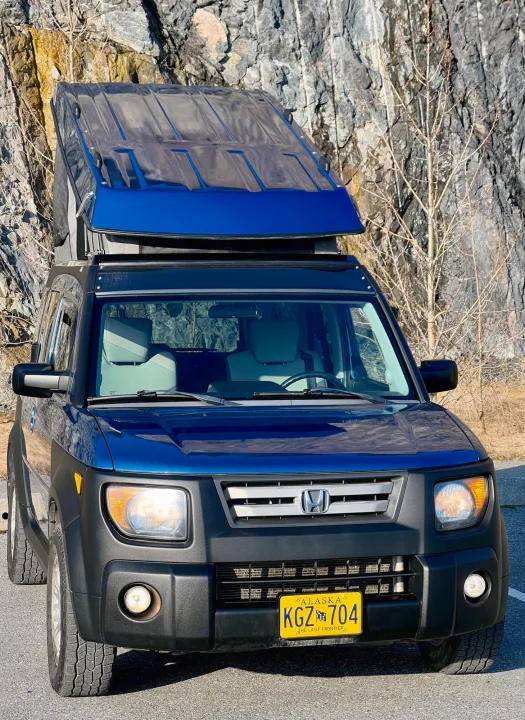 This blue Honda Element pop-top camper is an ideal RV rental for exploring Alaska. A compact camper van shown parked by rocks.. Honda Element Ecamper 2008