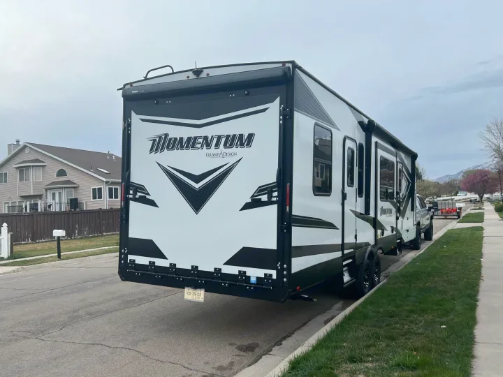 This large white and black Grand Design Momentum toy hauler RV rental is parked on a suburban street.. Grand Design Momentum 2022