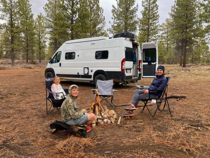 Family of three enjoys a campfire at their campsite with a white RV rental van. Perfect for outdoor adventures.. Winnebago Solis 59PX 2022
