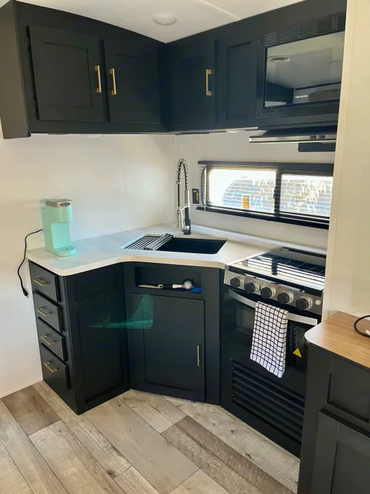 Sleek RV rental kitchen: black cabinets, light counters, sink, stove, microwave, and a Keurig. Modern, compact space.. Springdale 251bh 2022
