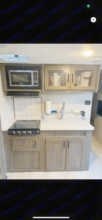 Compact RV rental kitchen featuring a modern microwave, cooktop, sink, and stylish wood-grain cabinets.. Shasta 25RS 2021