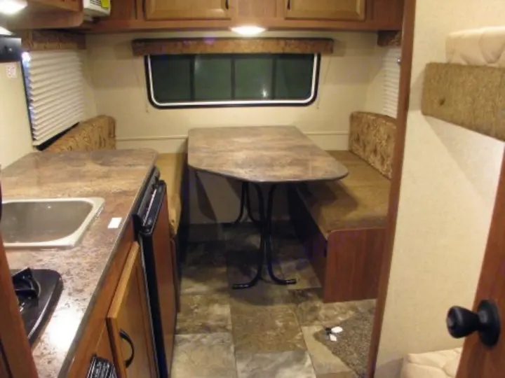RV rental interior: compact kitchen counter, dining table with bench seating, and visible bunk beds on the right.. Jayco Bambi 2014