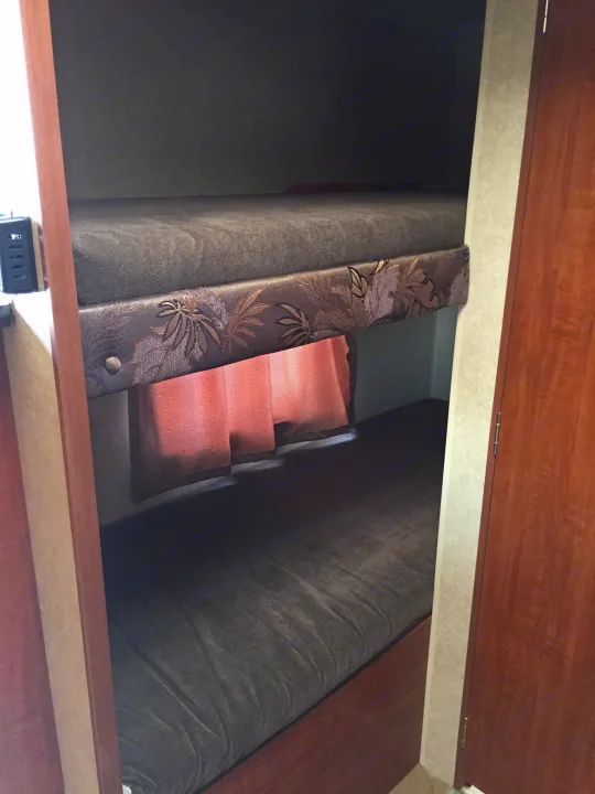 RV rental interior: narrow bunk beds with patterned bolster & soft pink steps. Cozy sleeping space.. Jayco Bambi 2014