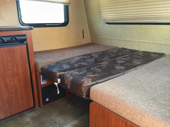 Cozy RV rental interior showing a convertible dinette bed with patterned and plain cushions, and a small kitchen.. Jayco Bambi 2014