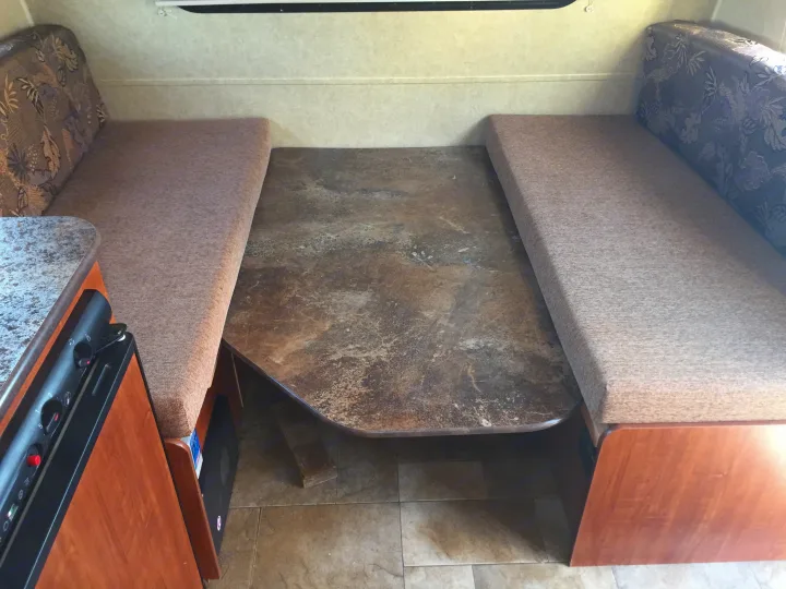 RV rental interior: A cozy dinette with patterned backrests, upholstered benches, and a mottled table surface.. Jayco Bambi 2014