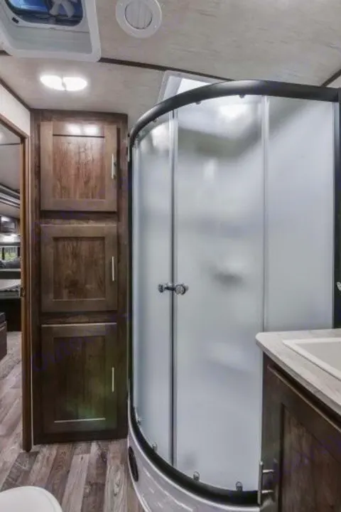 RV rental bathroom features a curved shower, vanity, and ample wood storage. Clean and functional travel space.. Radiance Big Bear 2020