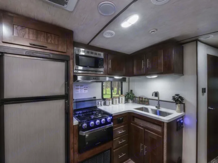 Explore this modern RV rental kitchen featuring a refrigerator, microwave, gas stove, sink, and sleek wooden cabinets.. Radiance Big Bear 2020