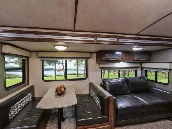 Comfortable **rv rental** interior: dining area, dark leather sofa, and windows showing lake and trees.. Radiance Big Bear 2020