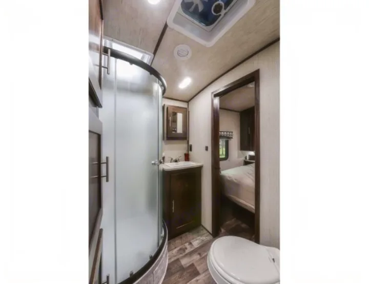 Compact RV rental bathroom features a curved shower, vanity with sink, toilet, and an adjacent bedroom view.. Radiance Big Bear 2020