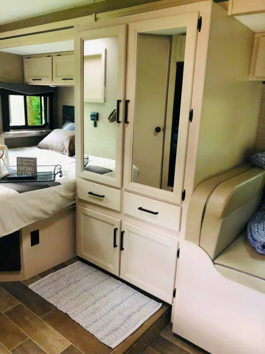 Clean RV rental bedroom interior featuring a comfortable bed, integrated mirrored storage, and cozy seating.. Thor Chateau 2022