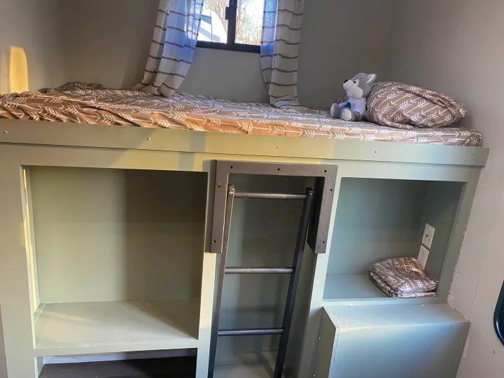 Compact RV rental bunk beds feature a cozy top bunk with arrow bedding, plush toy, window, and integrated lower storage with a ladder.. Gulf Stream Conquest 2015