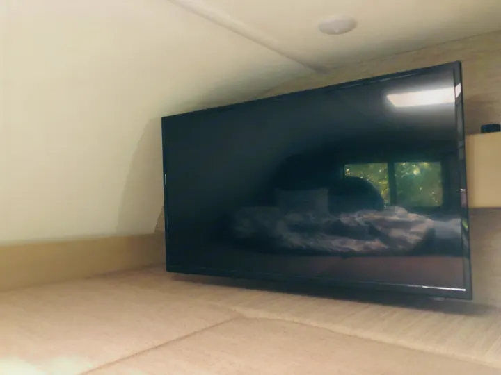 Enjoy entertainment in your RV rental! This TV screen reflects a cozy bedroom area with a window view inside a camper.. Thor Chateau 2022