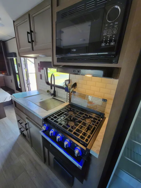 RV rental kitchen: modern microwave, stove with illuminated knobs, and sink in a compact interior.. Jayco Rocky Mountain Edition 2022