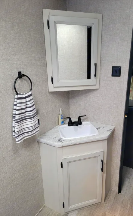 Compact RV rental bathroom features a light vanity, white sink, black faucet, mirror, and striped towel.. Jayco Rocky Mountain Edition 2022