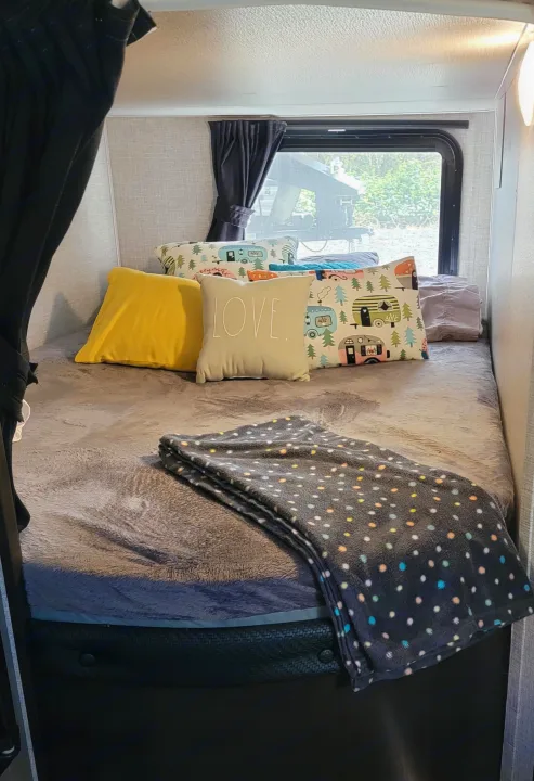 Cozy RV rental bedroom featuring a comfy bed with colorful camper-themed and 'LOVE' pillows, and a soft polka dot blanket.. Jayco Rocky Mountain Edition 2022