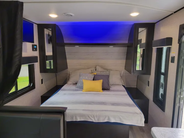 Relax in this modern RV rental bedroom. It features a comfortable bed, blue accent lighting, TV, and compact storage.. Jayco Rocky Mountain Edition 2022