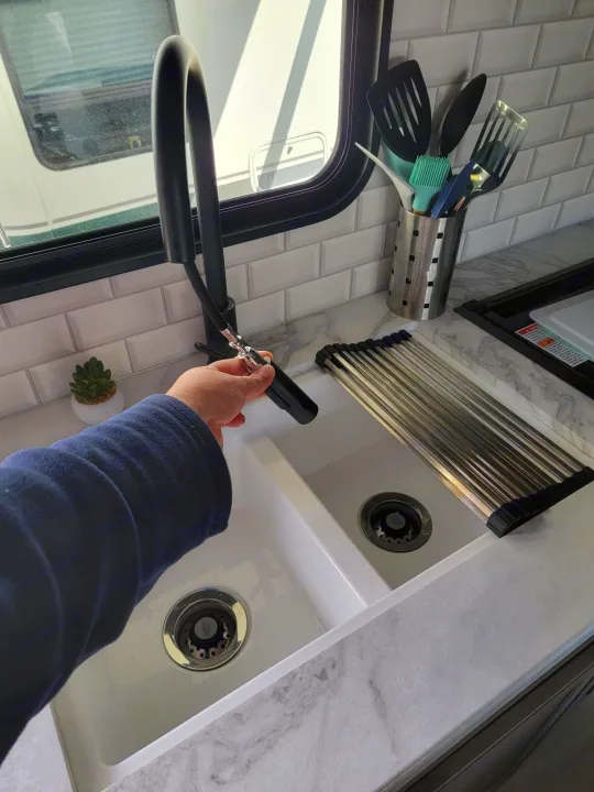 Inside an RV rental: a clean kitchen features a dual sink, pull-down faucet, tile backsplash, and drying rack.. Jayco Rocky Mountain Edition 2022
