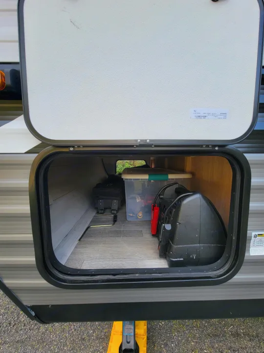 An open RV rental storage compartment shows a portable generator, clear bin with cables, and other travel essentials.. Jayco Rocky Mountain Edition 2022