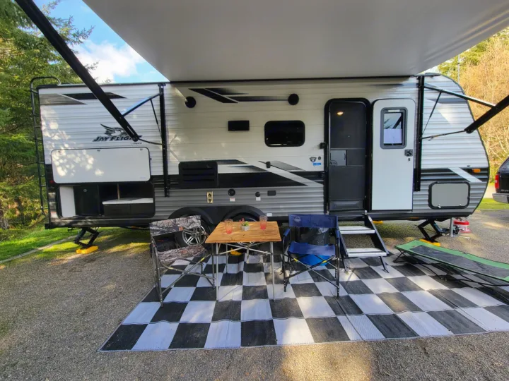 Cozy RV rental setup: a Jay Flight travel trailer with extended awning, chairs, and table on a checkered outdoor mat.. Jayco Rocky Mountain Edition 2022