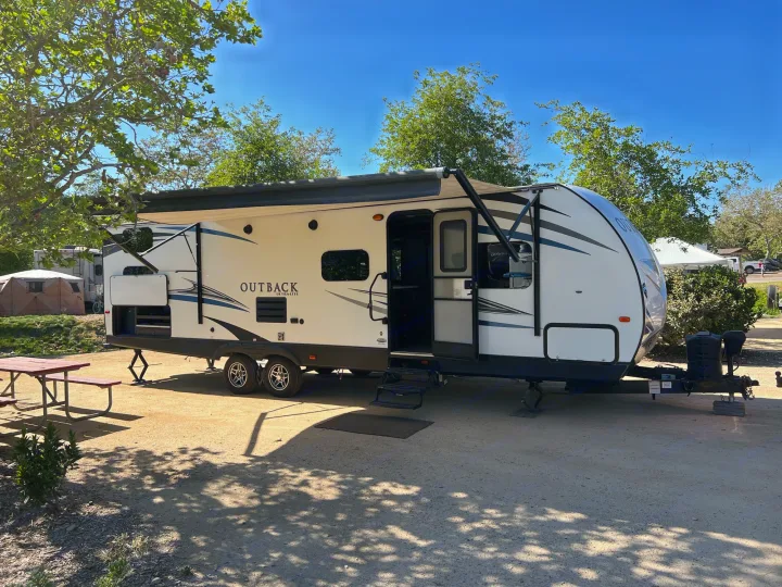 A white Outback travel trailer, an excellent rv rental option, is set up with awning extended at a sunny campsite.. Keystone Outback 2019
