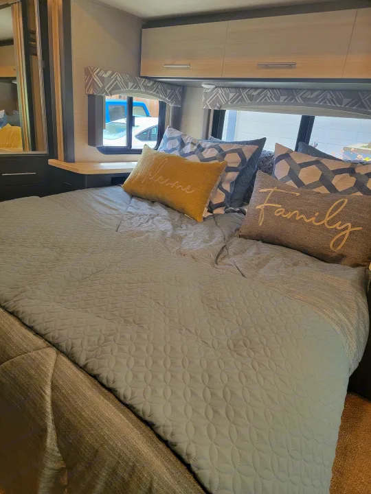 Experience comfort in this inviting RV rental bedroom. Features quilted bedding, decorative pillows, and stylish decor.. Thor Axis 2021