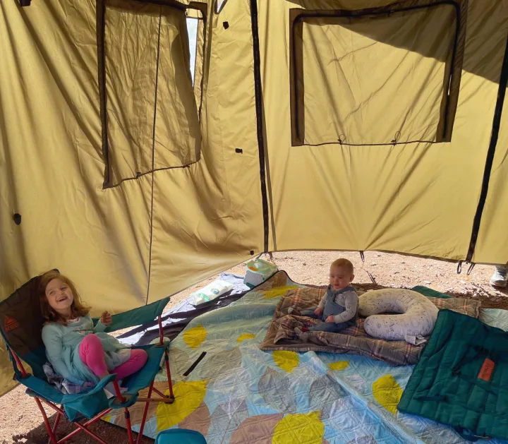 Inside a spacious RV rental tent, a girl and a baby relax on blankets. Cozy family camping fun!. Bean Mean Bean 2022