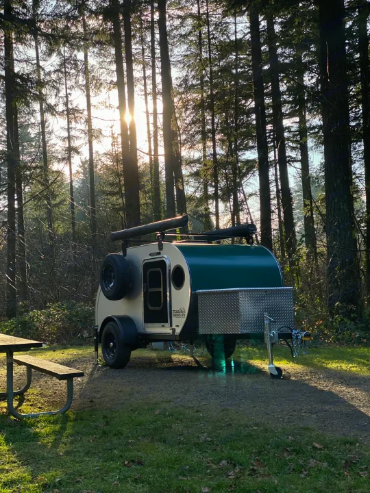 Teardrop camper trailer, ideal for an RV rental, parked in a sunlit forest campsite with a picnic table.. Teardrops Northwest Trek 2022