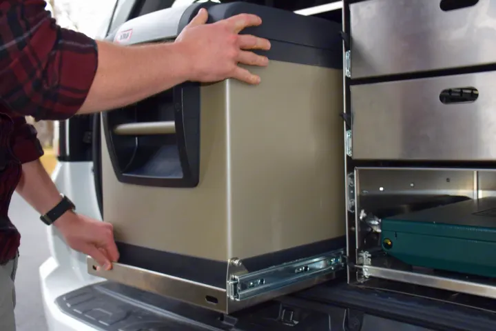 Someone slides a portable fridge into a vehicle's custom storage system, ideal for RV rental adventures.. Toyota 4Runner 2021