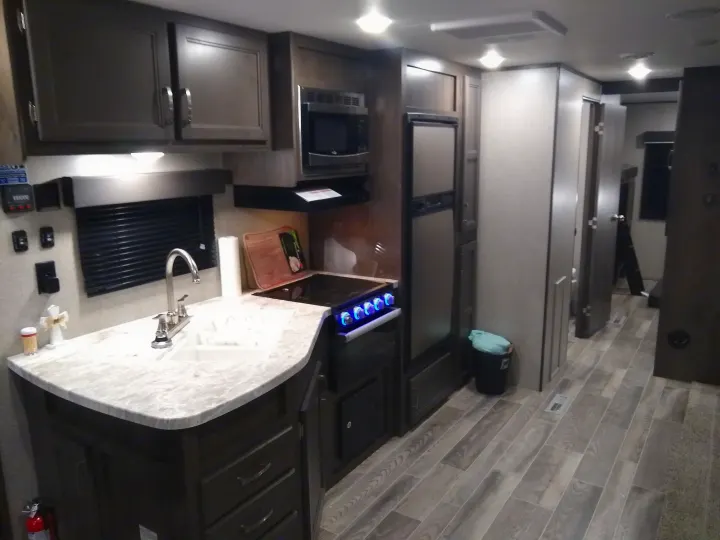 Inside a modern RV rental: A kitchen with dark cabinets, light counters, sink, stove, microwave, fridge, and wood-look floors.. Jayco Jay Flight SLX 2021