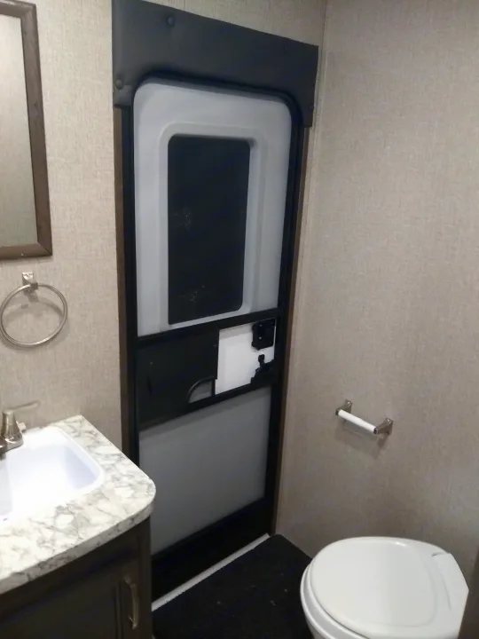 Inside an RV rental bathroom, featuring a compact sink, toilet, and an RV-style door with privacy screen.. Jayco Jay Flight SLX 2021