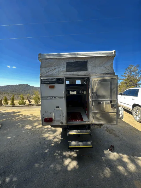 Pop-up LITE-CRAFT **rv rental** parked outdoors with door open & steps down, revealing interior. Mountains beyond.. Chevrolet Open Road 1998