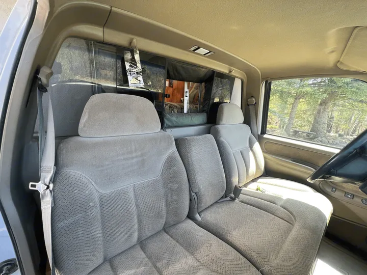 Bright RV rental interior: front seats offer a clear view into the rear camper conversion, with scenic trees outside.. Chevrolet Open Road 1998