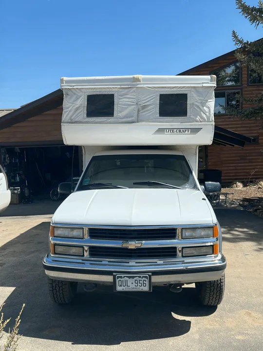 Front view of a white pickup truck with a LITE-CRAFT pop-up camper, parked in a driveway. Ideal for an rv rental.. Chevrolet Open Road 1998