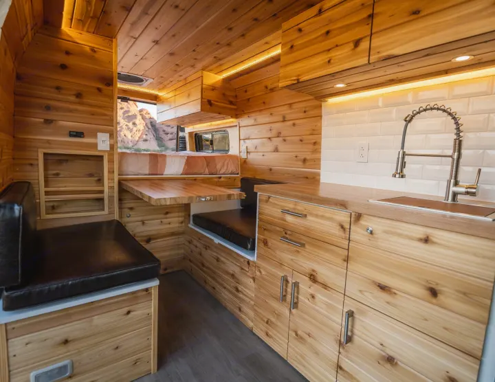 Custom RV rental interior with cedar wood panels, modern kitchen, seating, and bed area. Enjoy the outdoors in comfort!. Dodge Ram Promaster 2500 High Roof 159" 2021