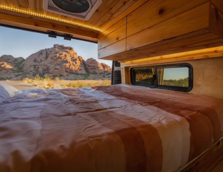 Cozy rv rental bed inside a wooden camper van, with warm lighting and a stunning desert mountain view.. Dodge Ram Promaster 2500 High Roof 159" 2021