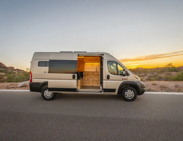 Explore this custom camper van's cozy wooden interior, ideal for an RV rental adventure. Parked at sunset in the desert.. Dodge Ram Promaster 2500 High Roof 159" 2021