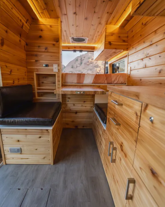 Cozy wood-paneled RV rental interior, featuring seating, table, storage, and scenic mountain views. Perfect for travel.. Dodge Ram Promaster 2500 High Roof 159" 2021