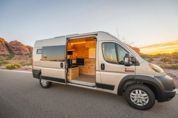 Champagne Ram ProMaster rv rental campervan with open door showing custom wood interior. Parked in desert at sunset.. Dodge Ram Promaster 2500 High Roof 159" 2021