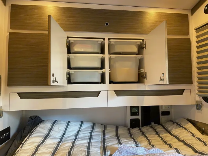 Organized RV rental bedroom with striped bed, open overhead cabinets revealing storage bins, and modern finishes.. Bean Mean Bean 2022
