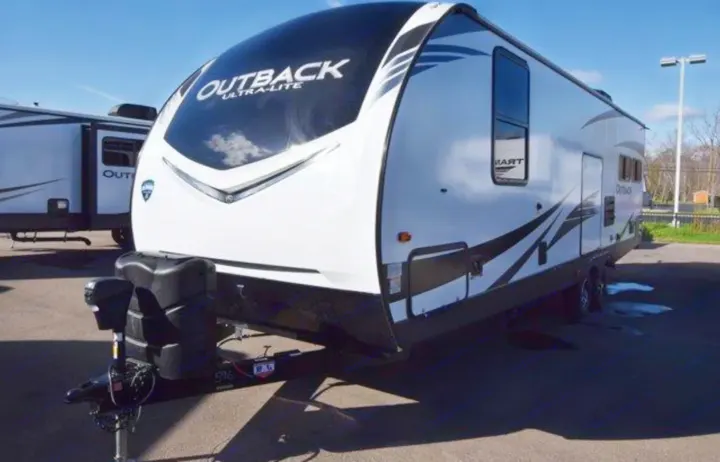 White 'Outback Ultra-Lite' travel trailer with black trim & hitch. Common rv rental type, shown outdoors.. Keystone RV Outback Ultra-Lite 2020
